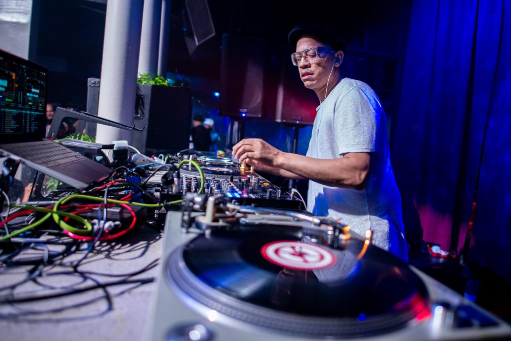 A DJ mixing live on turntables and a controller next to a laptop