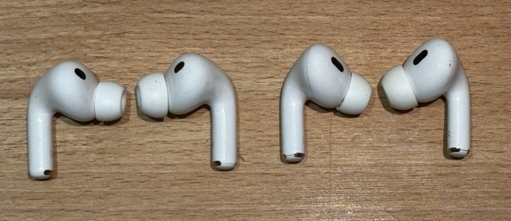 Two generations of Apple AirPods side by side on a dark reflective surface