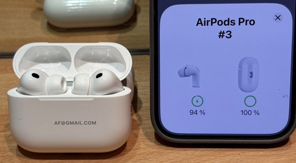 Two white AirPods Pro 3 earbuds resting on a reflective surface
