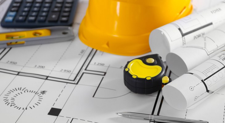 Construction blueprints with a tape measure, calculator and hard hat for project estimating