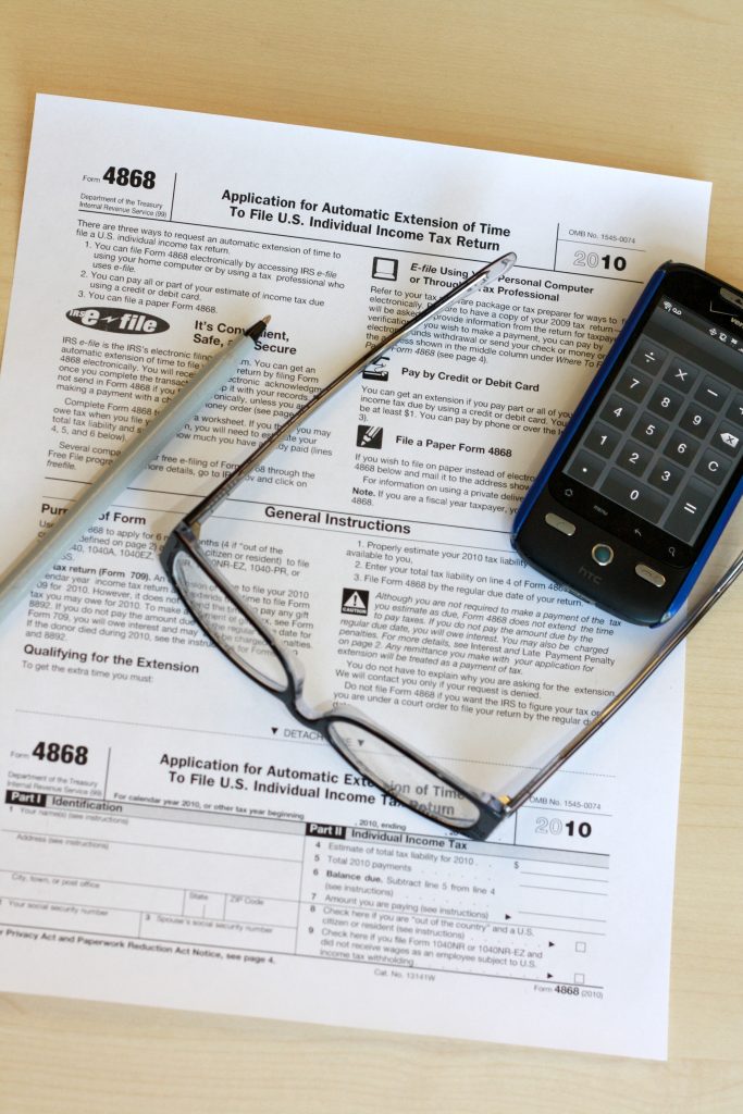 IRS Form 4868 tax extension form with glasses, pen, and phone