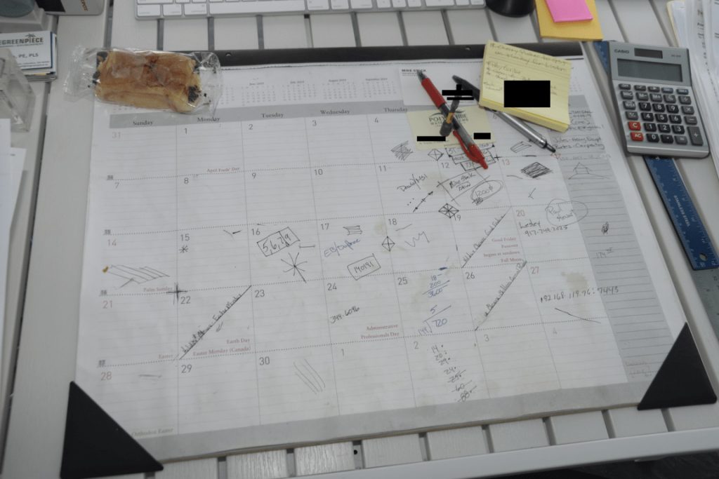 Executive assistant's desk planner covered in calendar notes, with calculator and sticky notes