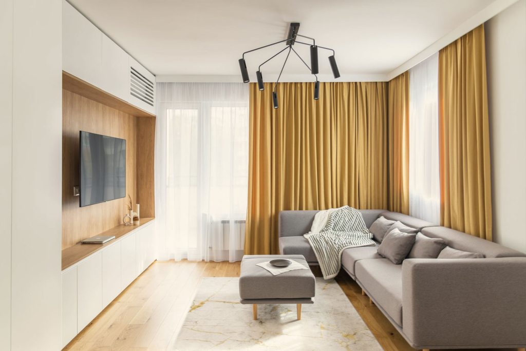 Modern living room interior with gray sofa, mustard curtains, and designer lighting
