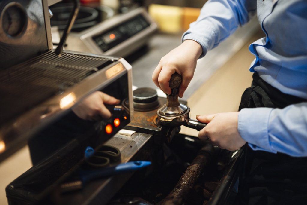 A barista tamping espresso grounds at a coffee shop espresso machine