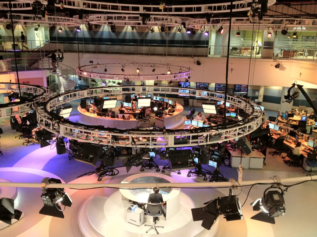 A television newsroom with journalists working at desks and studio lights