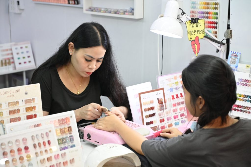 A nail technician filing a client's nails at a salon table surrounded by nail color samples