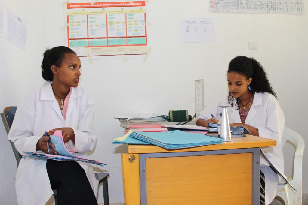 Nurses in white coats reviewing patient charts at a desk