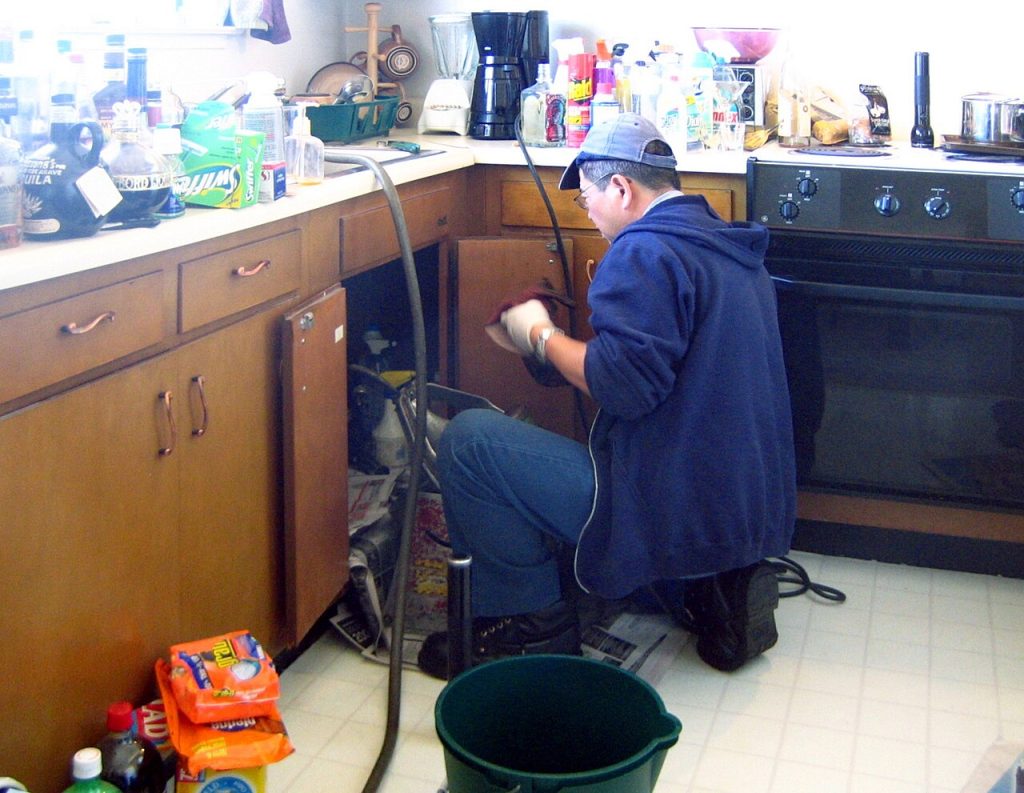 Plumber working on pipes under a kitchen sink